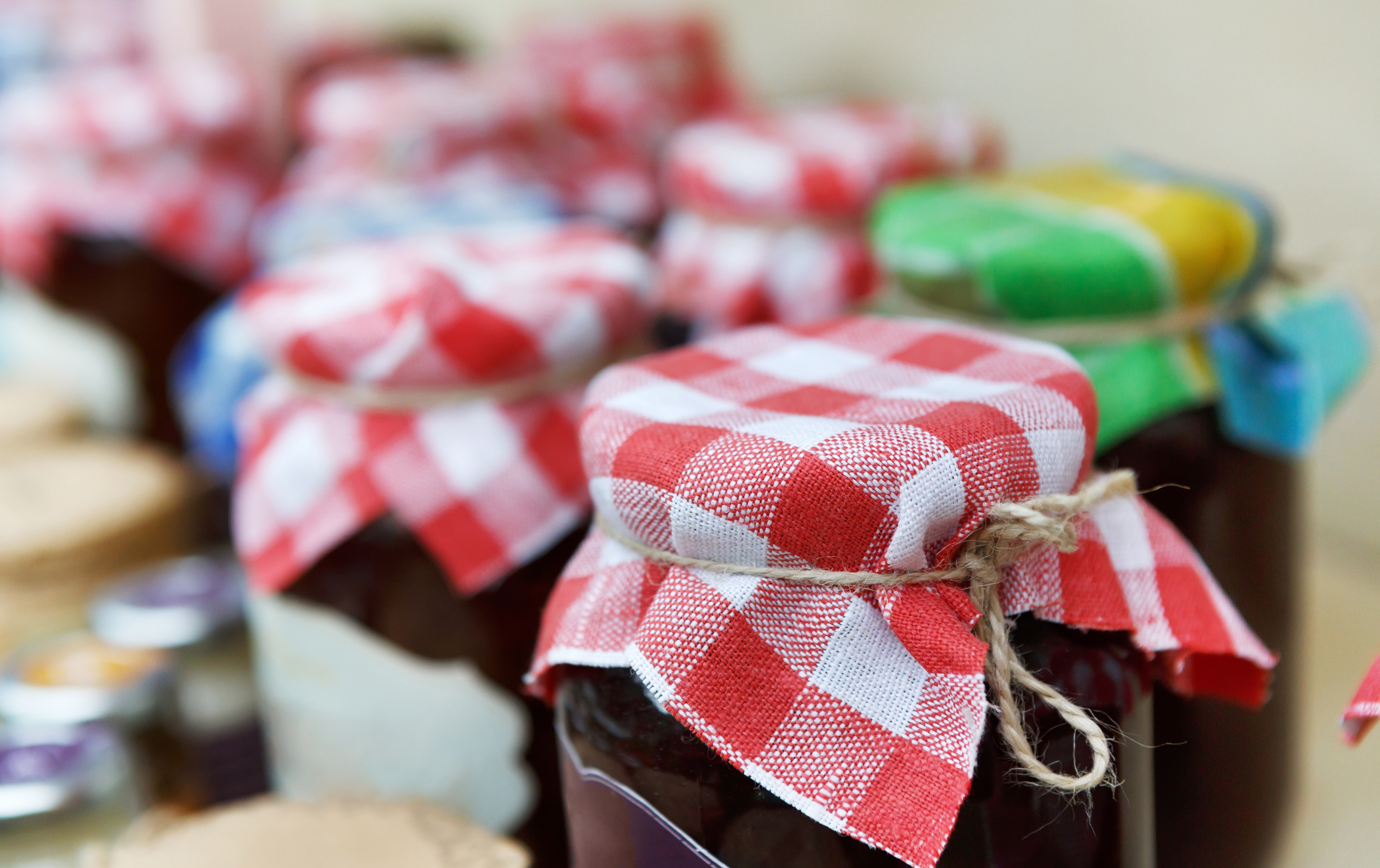 Jars of homemade jam lined up with plaid cloth tops.